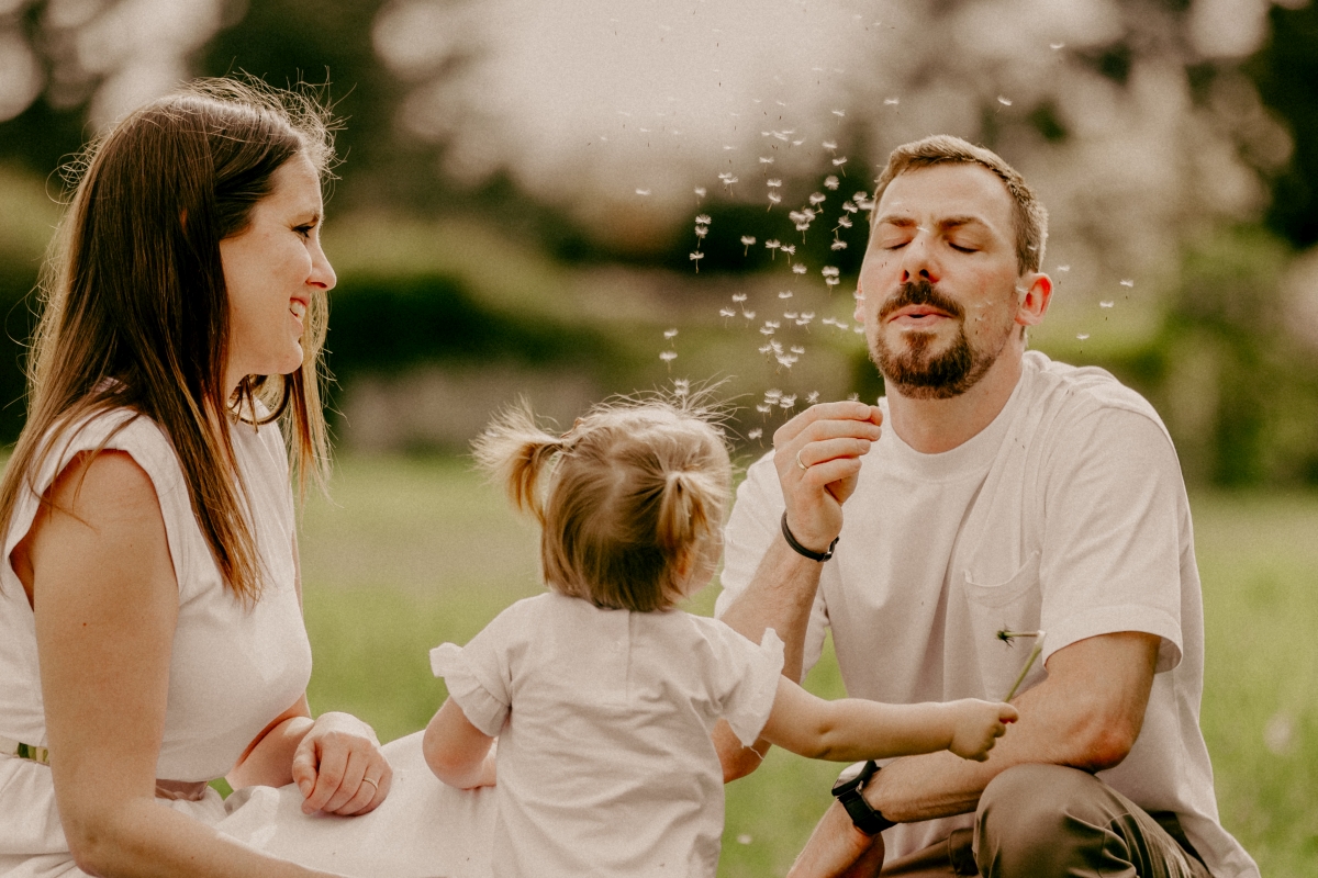 Papa mit Tochter mit Pusteblume auf Sommerwiesen beim Familien-Fotoshooting