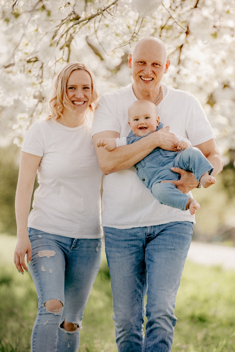 Mama und Papa mit Baby im Frühling unter Kirschblüten beim Familien-Fotoshooting