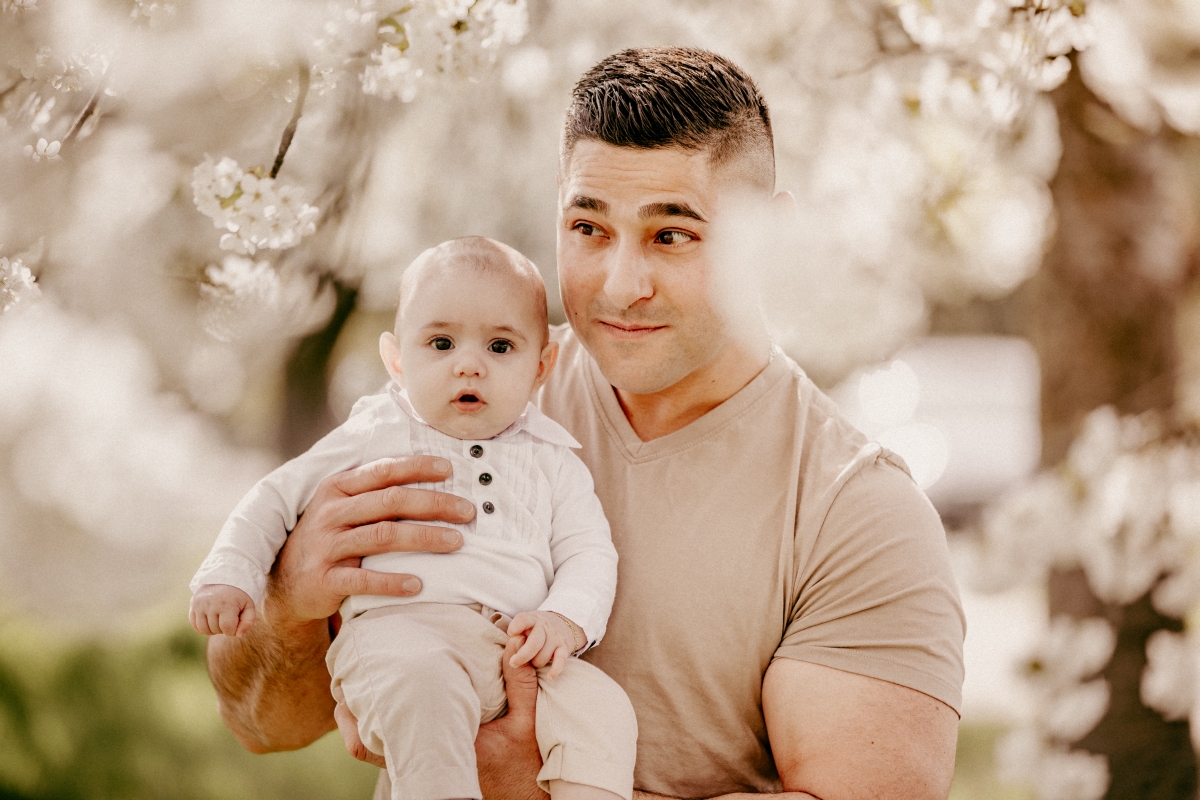 Papa mit Baby im Frühling unter Kirschblüten beim Familien-Fotoshooting