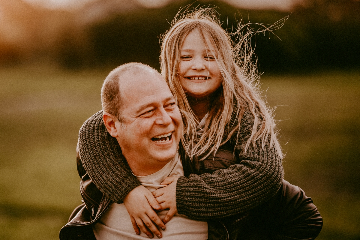 Vater und Tochter lachend Huckepack im Sonnenuntergang beim Foto-Shooting in der Natur