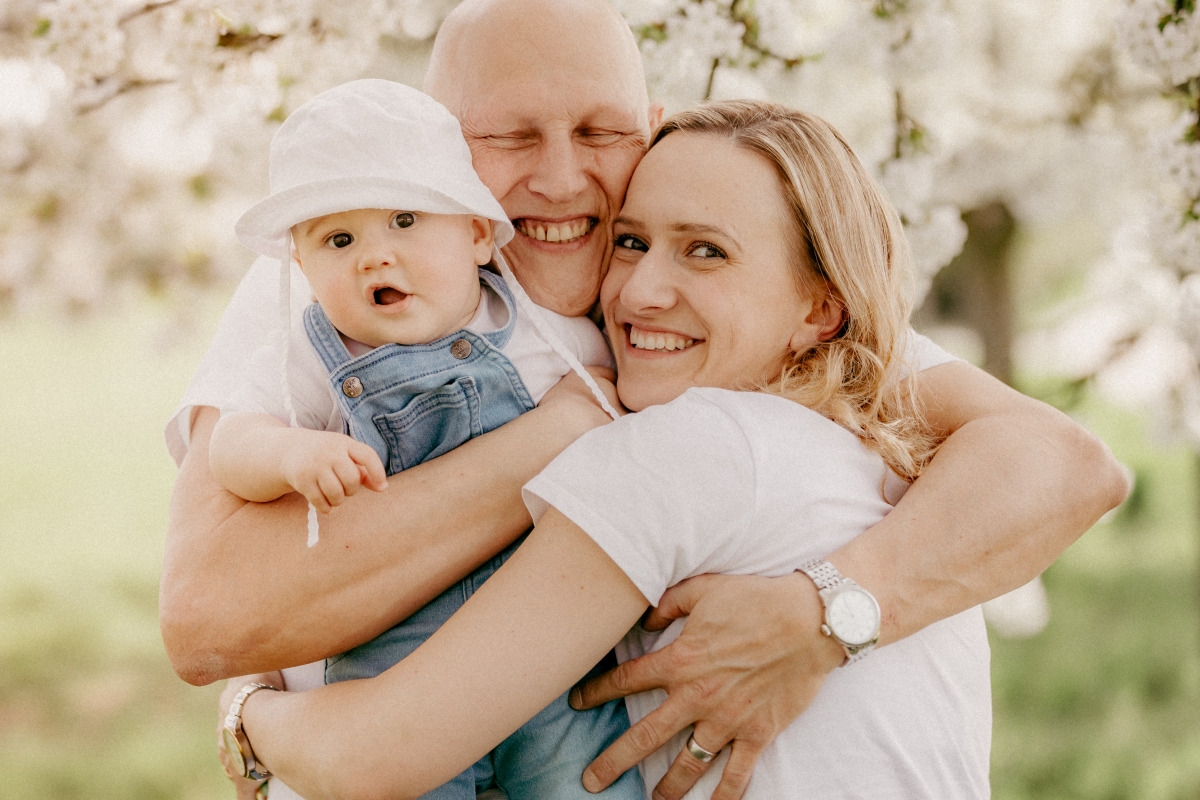 Mama und Papa mit Baby im Frühling unter Kirschblüten beim Familien-Fotoshooting