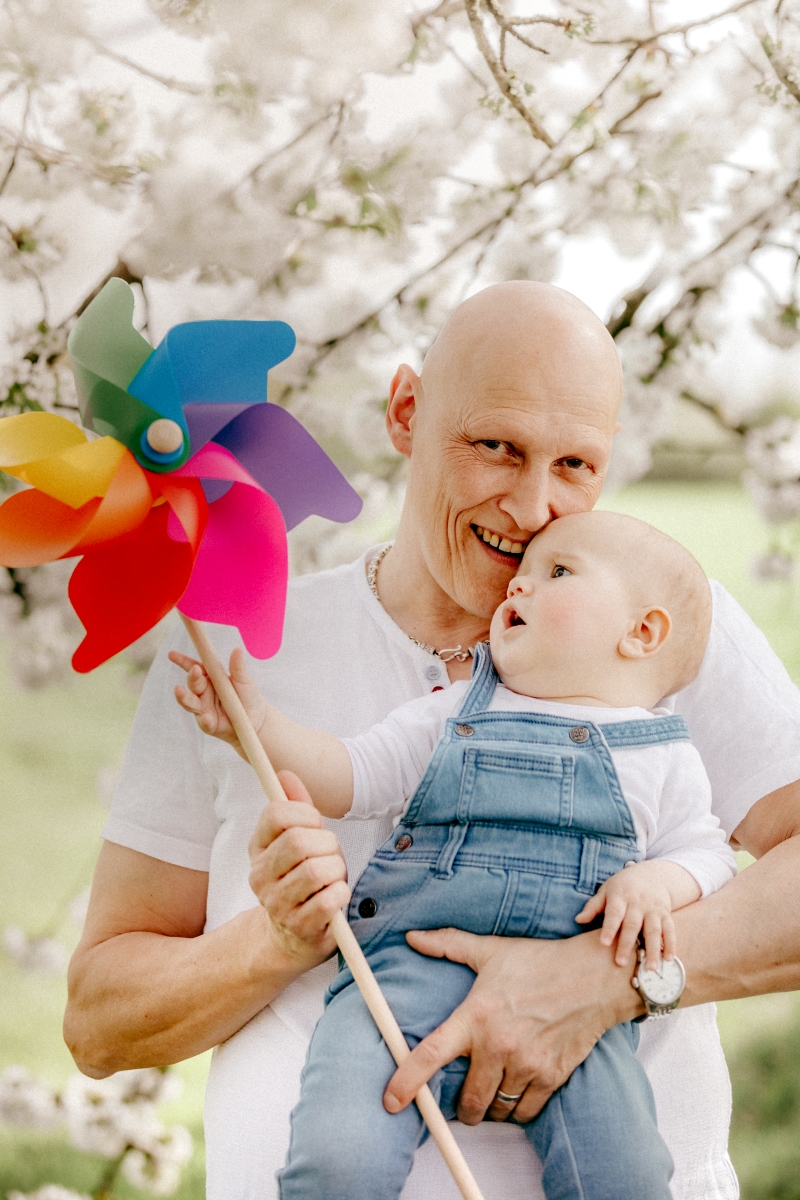 Papa mit Baby udn Windrad  im Frühling unter Kirschblüten beim Familien-Fotoshooting