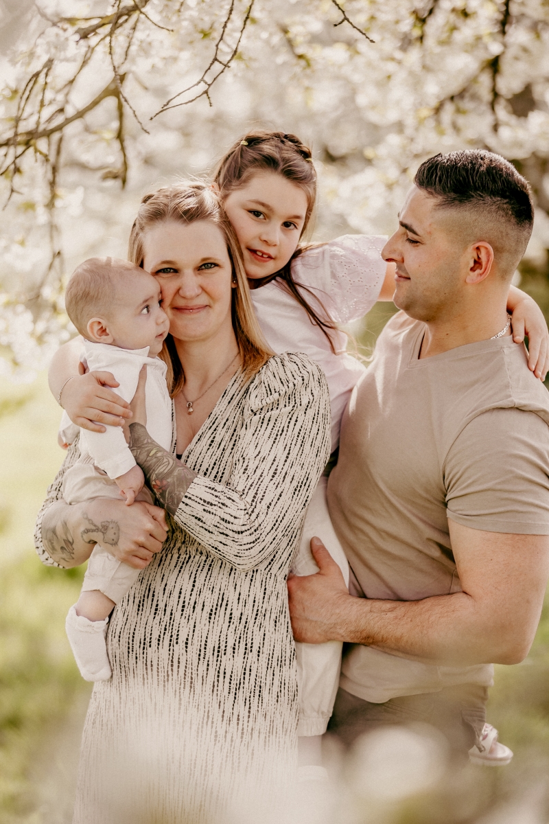 Mama und Papa mit Baby und Mädchen im Frühling unter Kirschblüten beim Familien-Fotoshooting