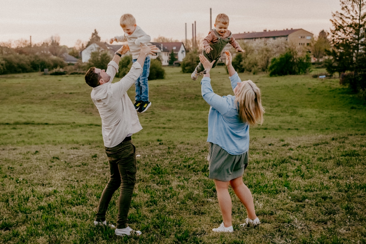 Eltern mit Kindern auf den Schultern auf der Sommerwiese beim Familien-Fotoshooting