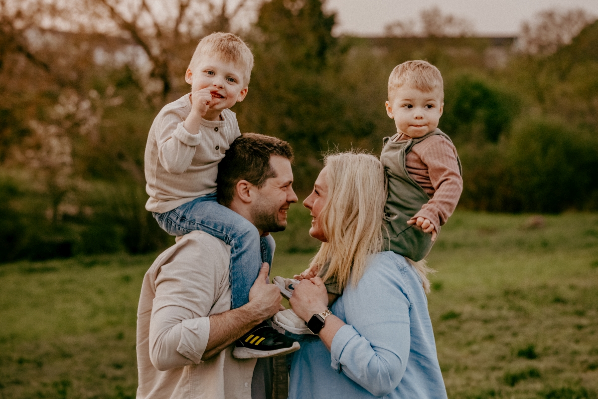 Eltern mit Kindern auf den Schultern auf der Sommerwiese beim Familien-Fotoshooting